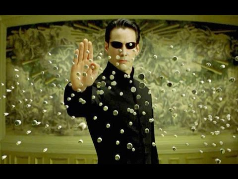 A photo from the Matrix, of a man holding up his hand while bullets freeze in the air in front of him.